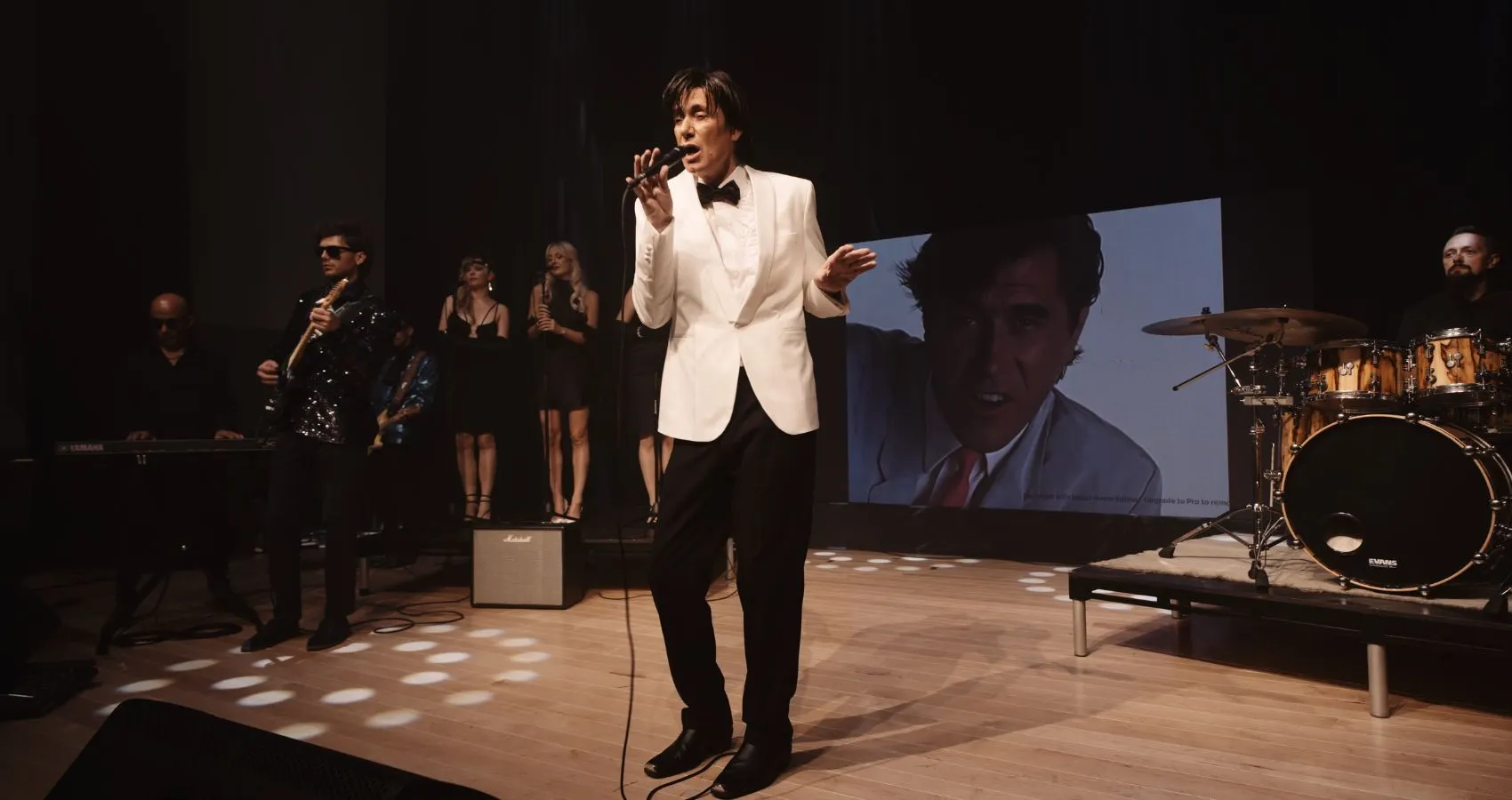 Sam Stevens in a white jacket with the band and backing singers