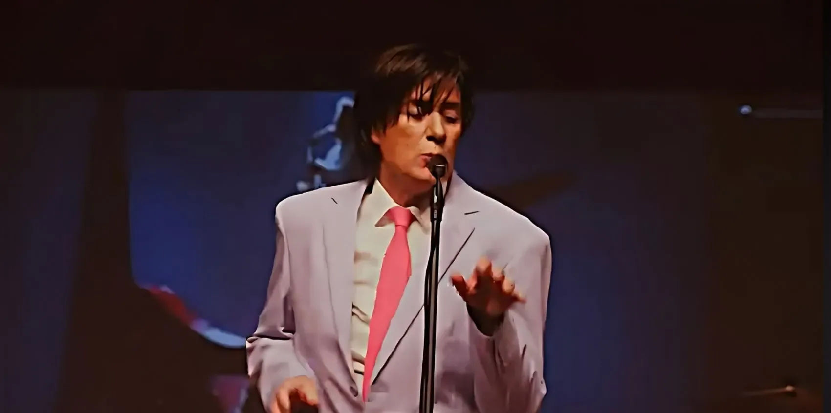 Sam Stevens singing in a pale suit and pink tie