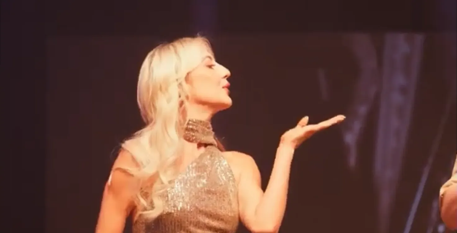 A vocalist in a gold dress blowing a kiss