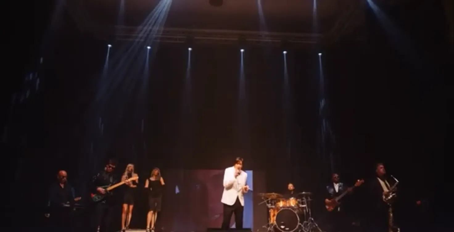 The full band on a theatre stage under spotlights