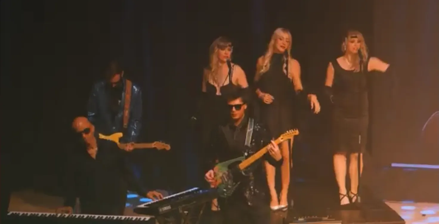 Guitarists and keyboard player in front of three backing singers in black dresses