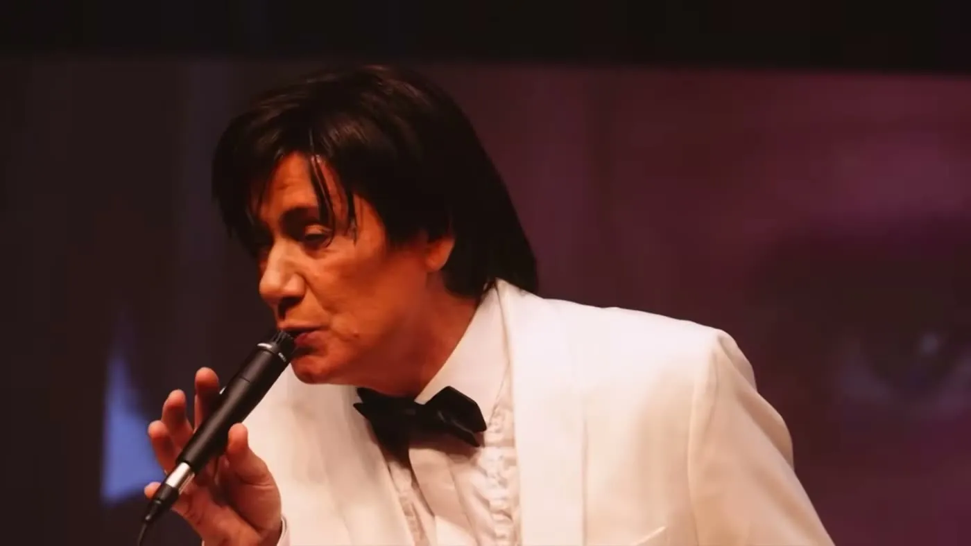 Sam Stevens singing in a white dinner jacket and bow tie